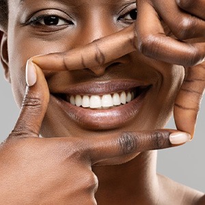 Woman smiling and forming her fingers as a box that outlines her teeth