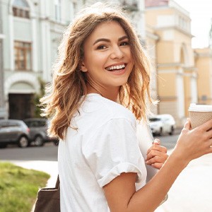 Young woman smiling as she’s walking with a coffee