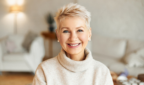 An older woman wearing a sweater and smiling, showing off her restored smile because of dental crowns