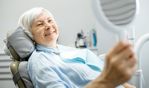 older woman admiring her smile with dentures in Newton 