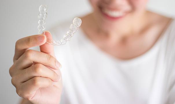 Woman holding Invisalign clear aligner with focus on aligner